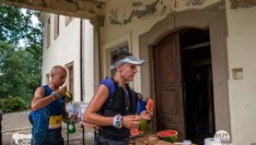 Dwoje biegaczy posilajacy się na tle ściany budynku z drzwiami
