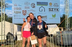 Panie stojące na podium dla zwycięzców na tle banera
